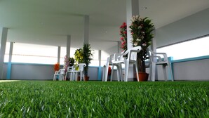 A room with artificial grass flooring, white plastic chairs, and potted plants.