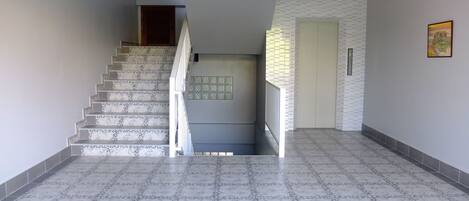 Una escalera conduce a un rellano con una puerta, suelo de baldosas y un aplique de pared.