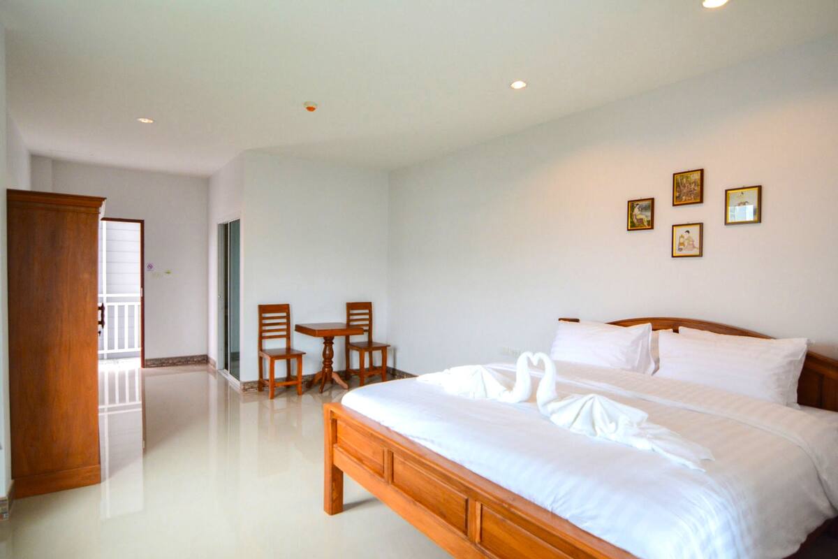 Quarto com cama grande, mesa de cabeceira de madeira, duas cadeiras e uma pequena mesa.