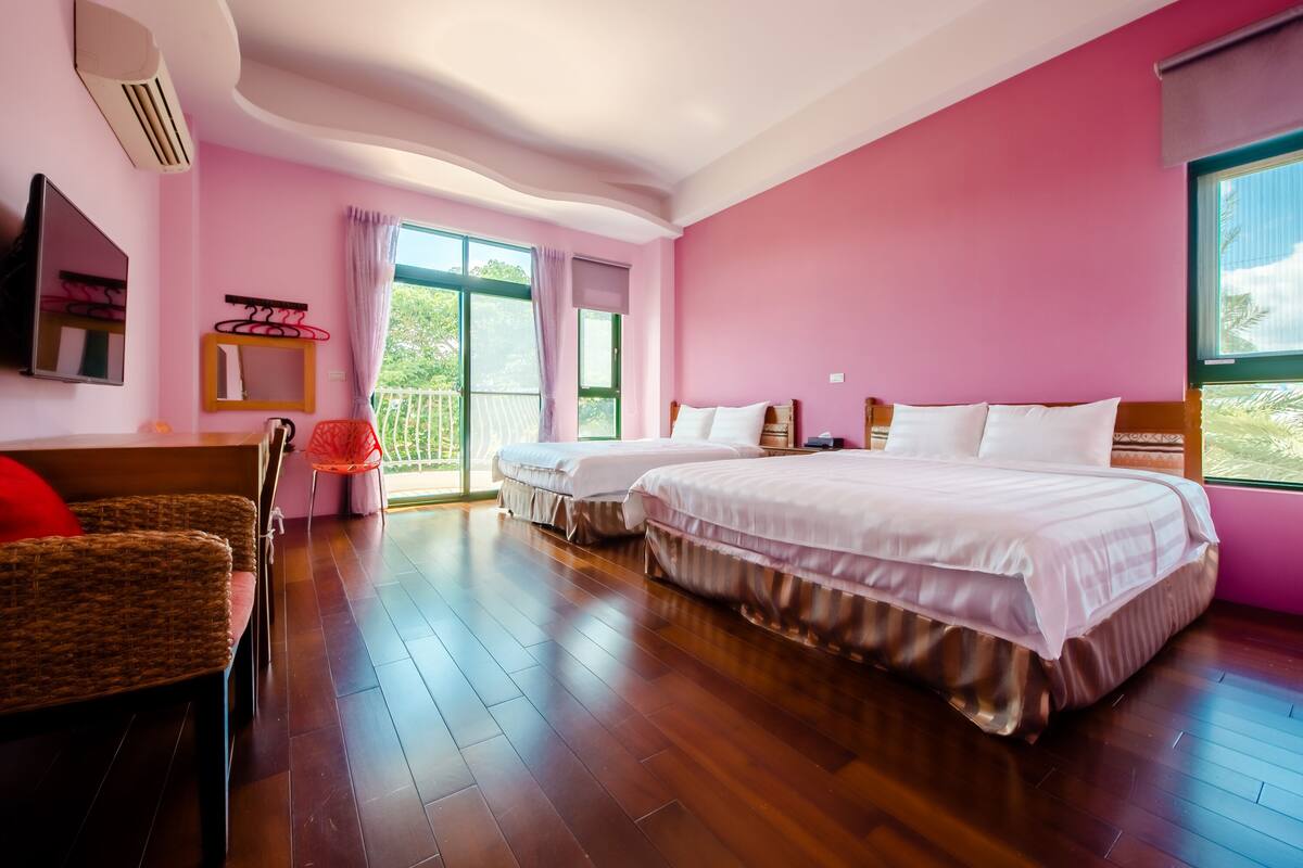 A hotel room with two beds, a wooden floor, a large window with a view, a TV, and a chair.