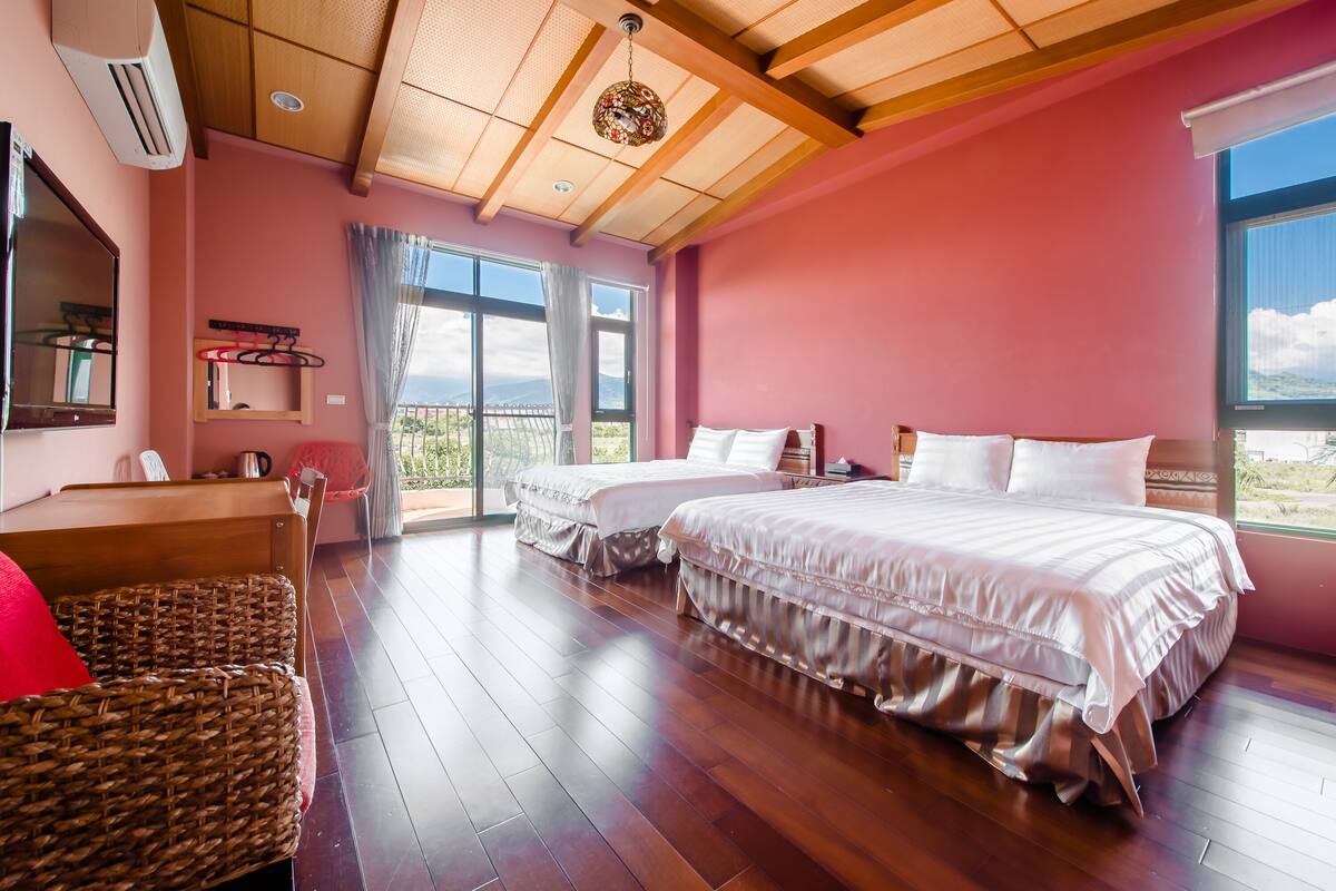 A bedroom with two beds, a wooden floor, a large window, and a balcony.