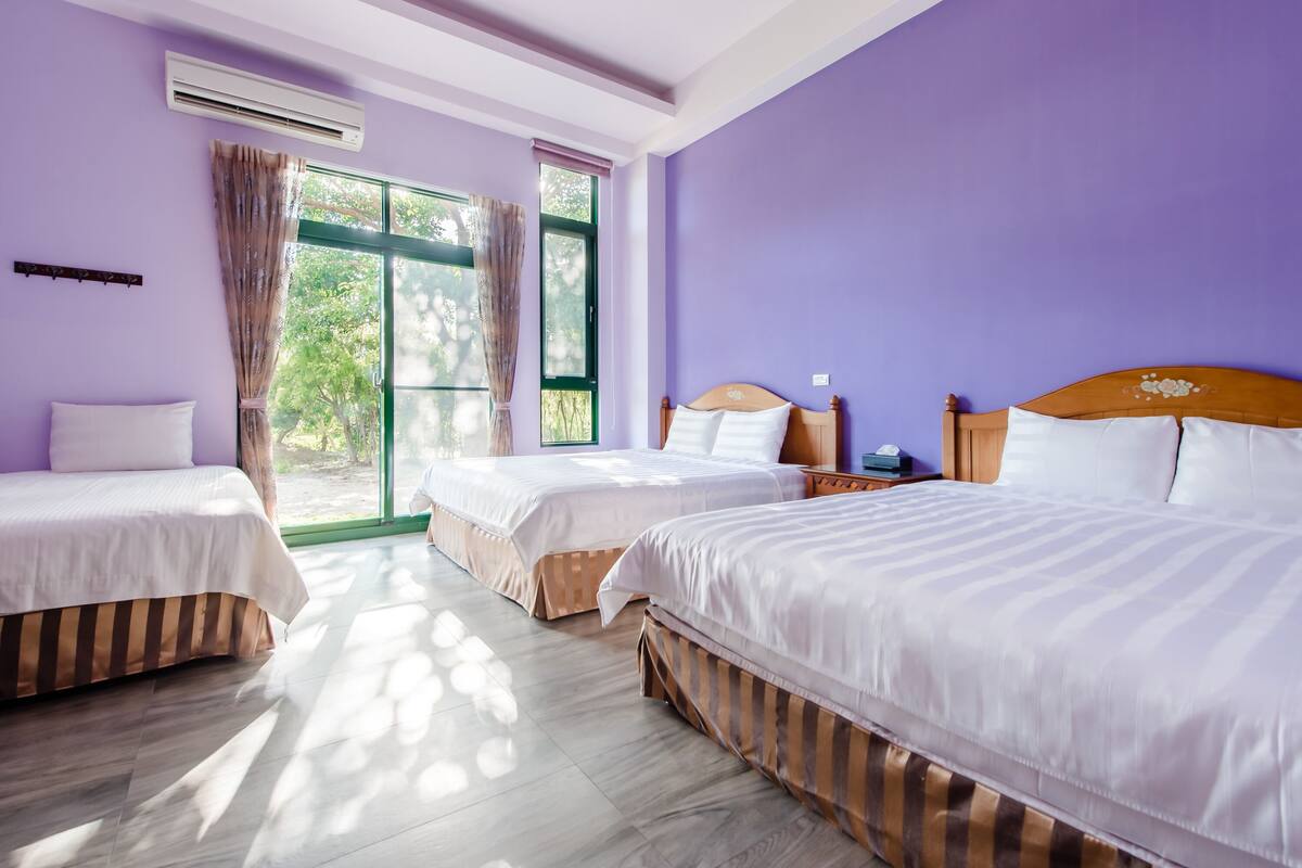 A room with three beds, large windows, and an air conditioning unit.