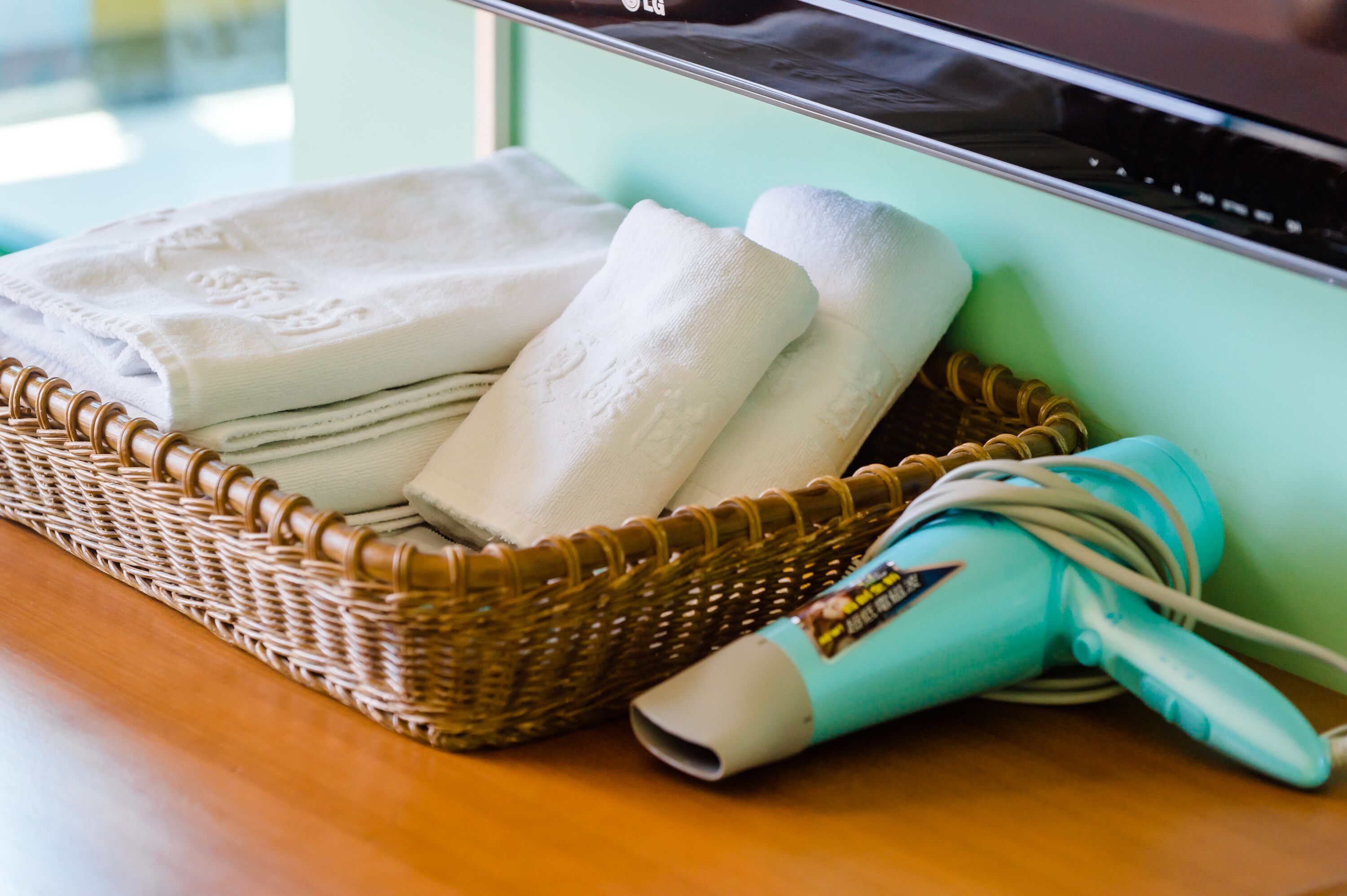 A wicker basket with folded towels and a hairdryer on a wooden table.