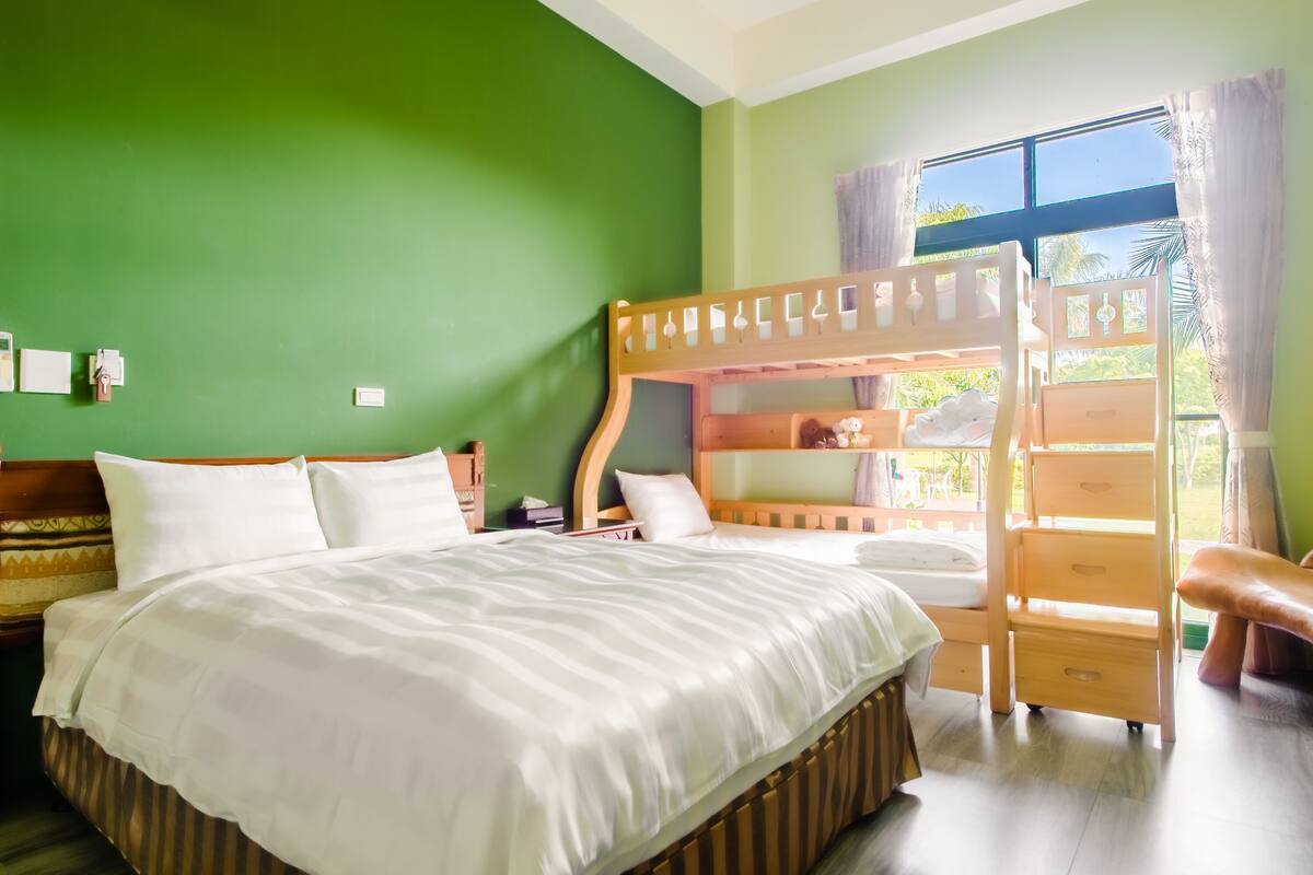 A room with a bunk bed, a single bed, a wooden nightstand, and a window with curtains.