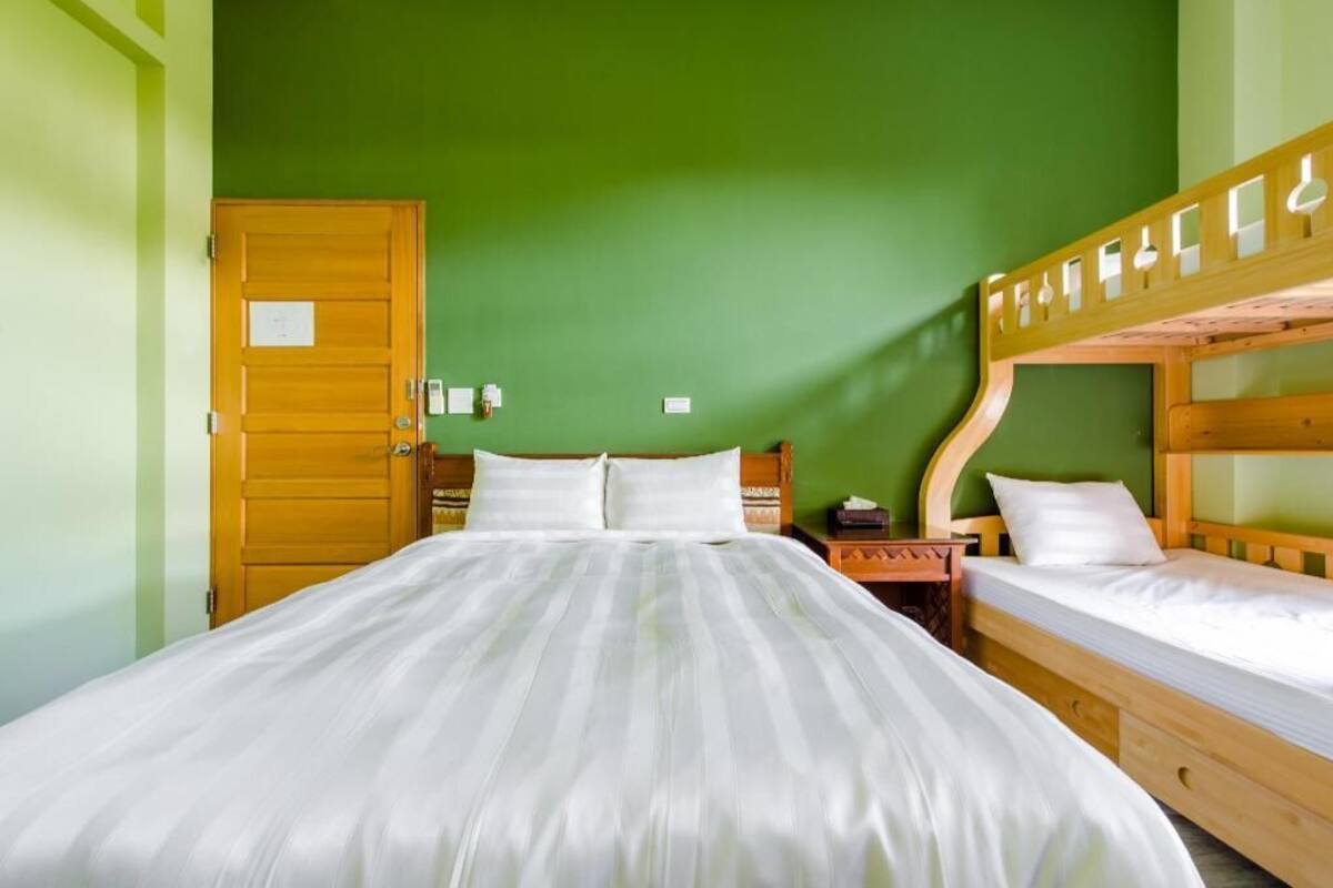 A room with a large bed, a wooden bunk bed, a door, and a nightstand.