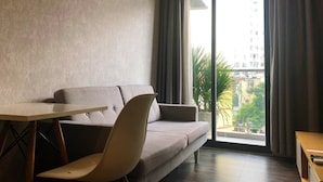 A modern living room with a sofa, a small table, and a view of a building through a large window.