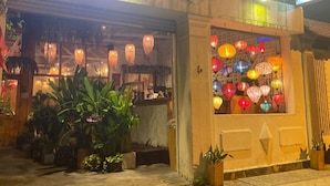 A restaurant with a neon sign, outdoor seating with plants, and colorful lanterns.