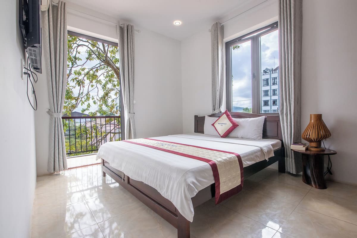 A hotel room with a bed, a bedside table with a lamp, and a window with curtains.