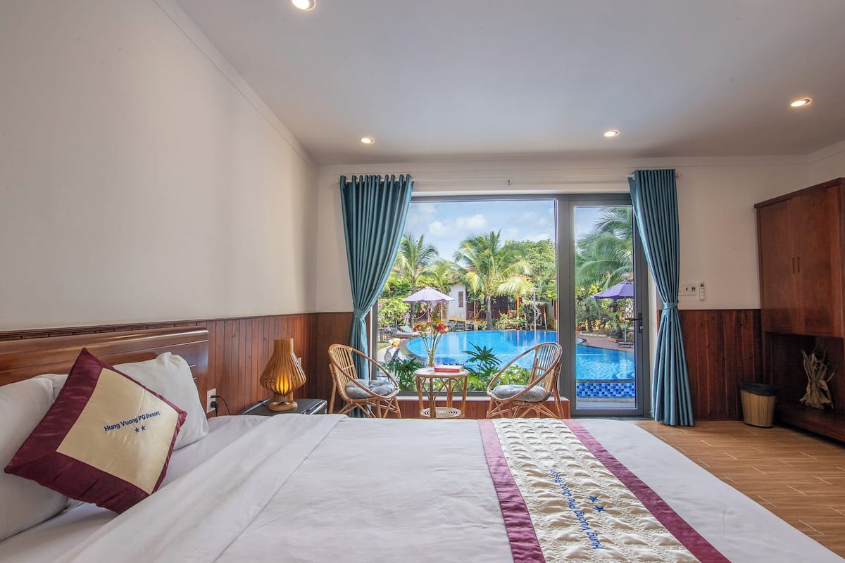 A hotel room with a bed, a view of a swimming pool, and a table with chairs.