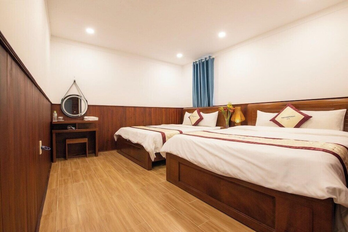 Ein Hotelzimmer mit zwei Betten, einem Nachttisch mit Spiegel, einem kleinen Tisch mit Blumenvase und einem blauen Vorhang.