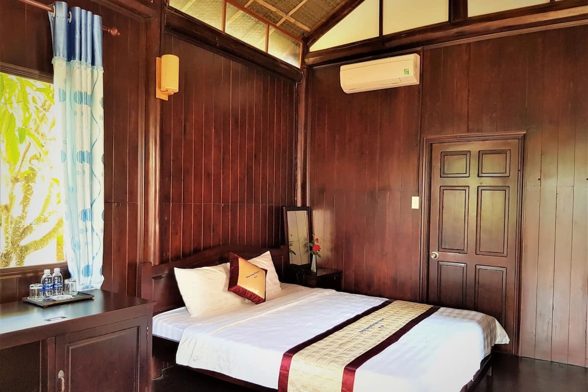 A wooden-paneled room with a bed, a desk, a mirror, and an air conditioning unit.