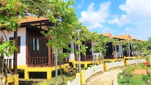 Une rangée de bâtiments de style colonial aux couleurs jaune et blanc, dotés de balcons, ainsi qu’un chemin pavé et une végétation luxuriante.