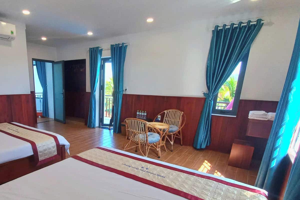 A hotel room with two beds, a dining area with chairs, and a view of the outdoors.