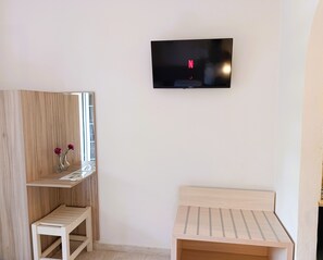 A room with a TV mounted on the wall, a wooden shelf with a mirror and vases, and a small wooden table. - Ever Green (Corfu)