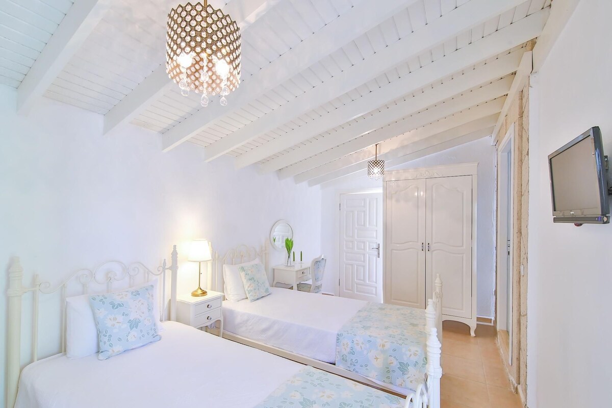 A bedroom with two beds, a chandelier, a mirror, and a wardrobe.