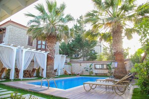 A pool area with lounge chairs, a stone building, and palm trees. - Alacati Balbadem Otel ( +13 ADULT ONLY) (Cesme)