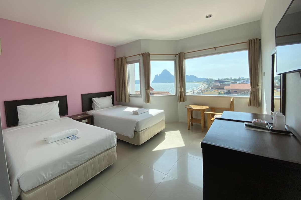 Quarto de hotel com duas camas, uma escrivaninha e vista para o mar e montanhas.