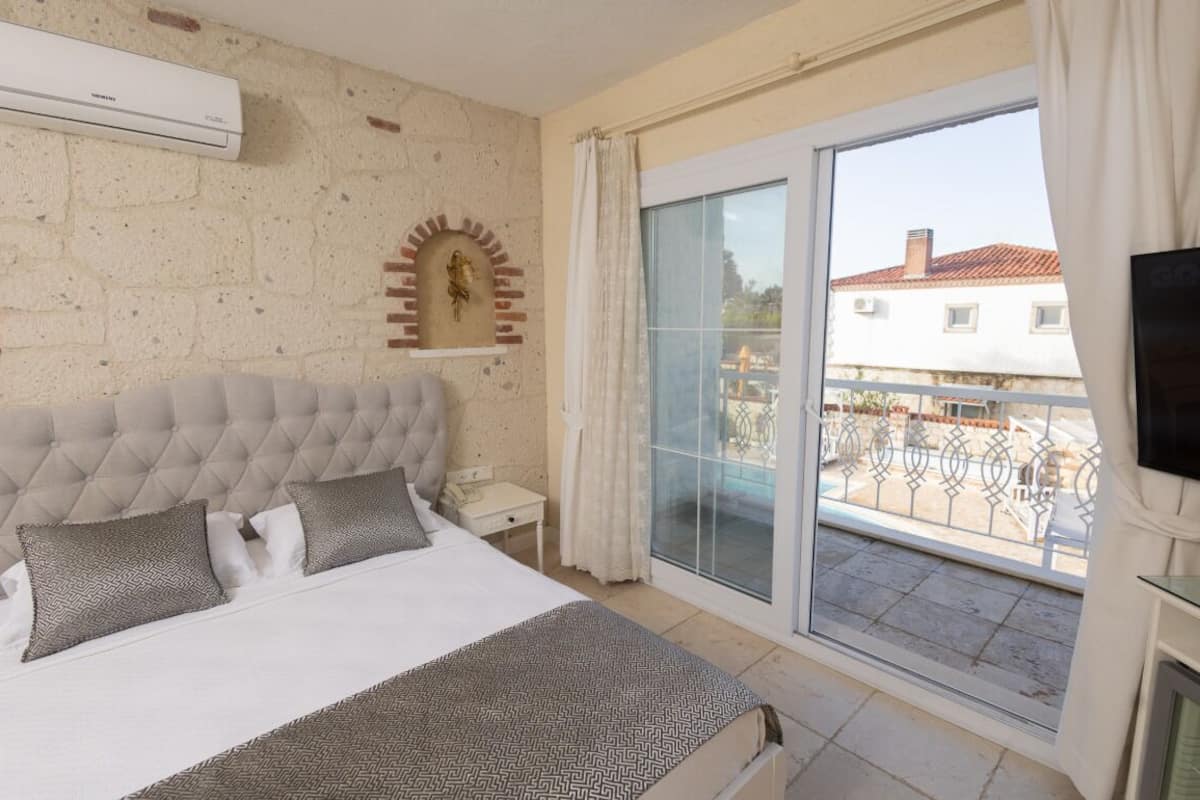 Quarto com cama grande, TV, porta de correr para uma varanda e parede de tijolos.