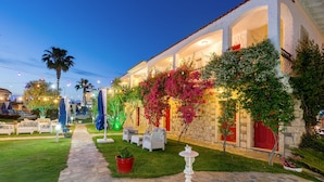 A courtyard with outdoor seating, a stone pathway, and a building with red doors and white walls. - Alaroof Hotel  ( +15 ) (Cesme)