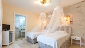 A bedroom with two beds, a television, a desk, and a bathroom visible through a glass door. - Alaroof Hotel  ( +15 ) (Cesme)