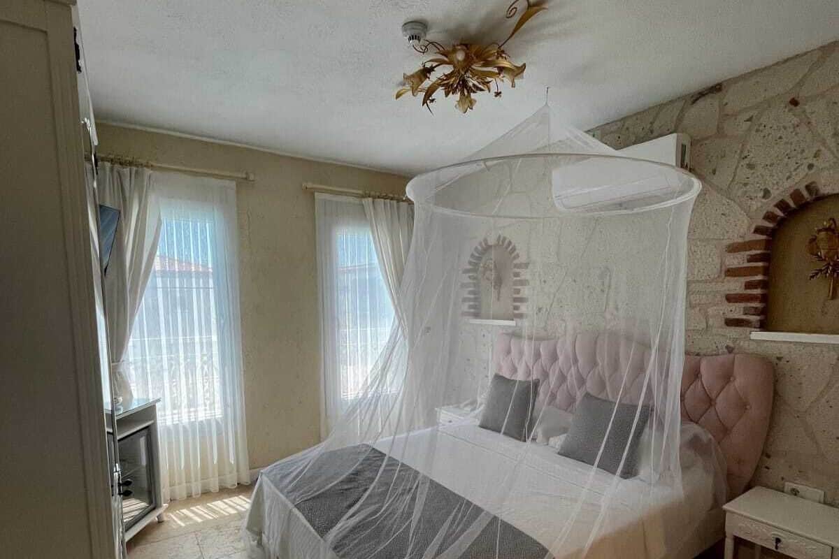 Quarto com cama sob dossel, mesa de cabeceira, cômoda e parede de pedra.