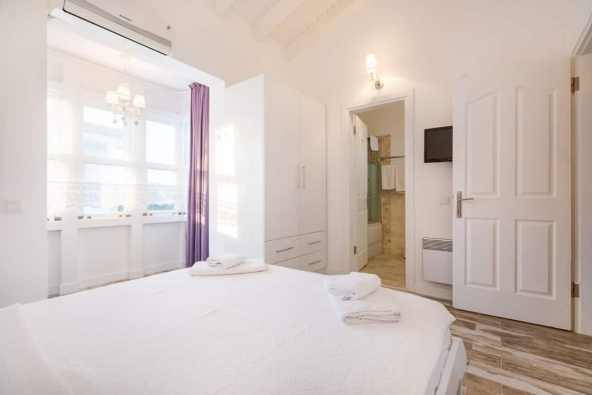 Quarto moderno com cama grande, closet espaçoso e banheiro visível através de uma porta aberta.
