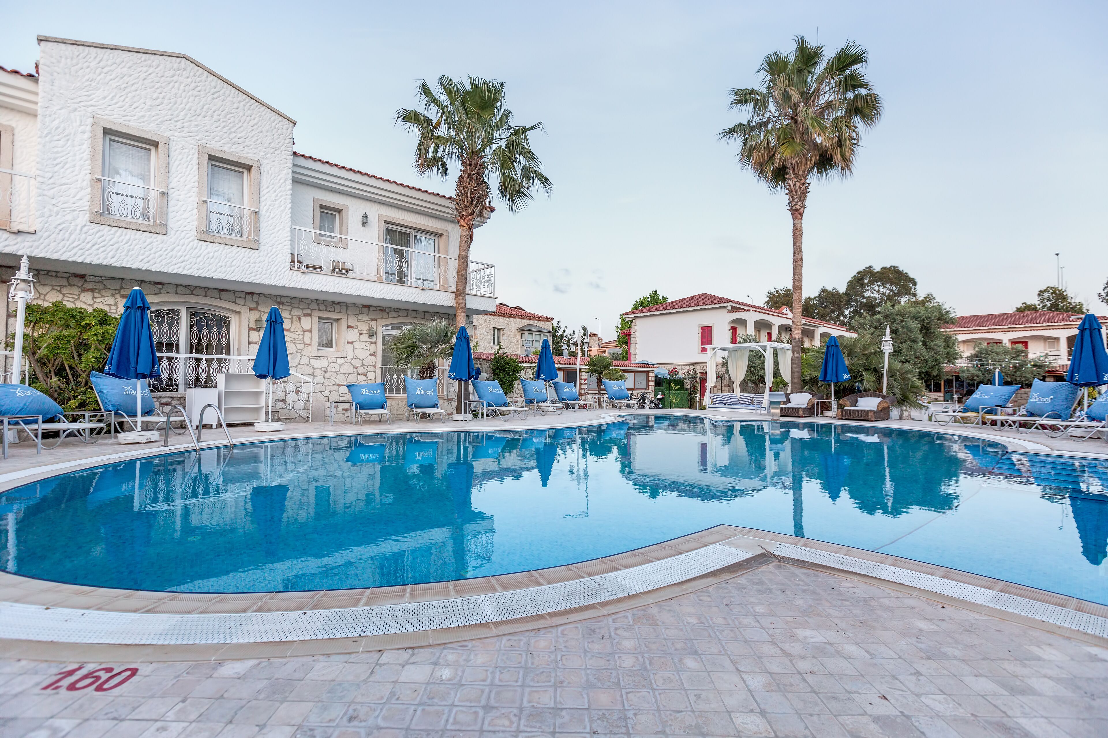 A swimming pool with lounge chairs and umbrellas, surrounded by stone buildings with balconies.