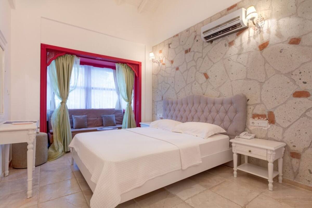 Quarto com uma cama grande, mesa de cabeceira, cortinas numa janela e ar condicionado fixado na parede.