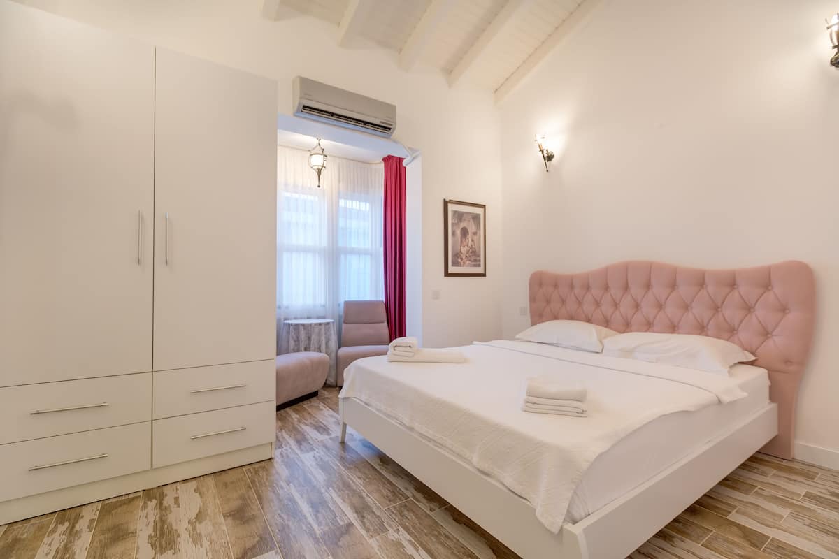 Quarto com cama grande, guarda-roupa, cadeira e pequena mesa.