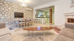 A modern living room with a stone wall, a flat-screen TV, a wooden coffee table, and a fireplace. - Alaroof Hotel  ( +15 ) (Cesme)