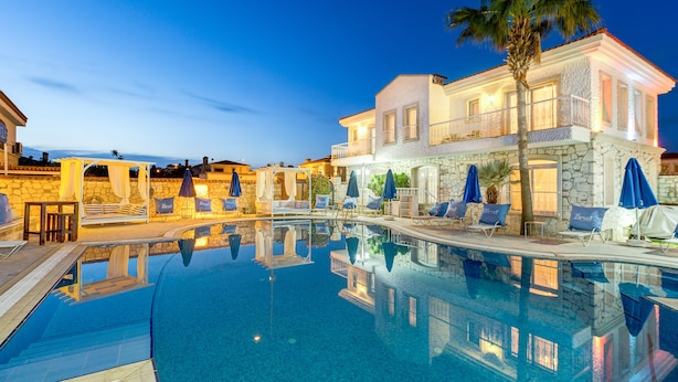 A swimming pool with lounge chairs and umbrellas, a stone building with a balcony, and a palm tree. - Alaroof Hotel  ( +15 ) (Cesme)