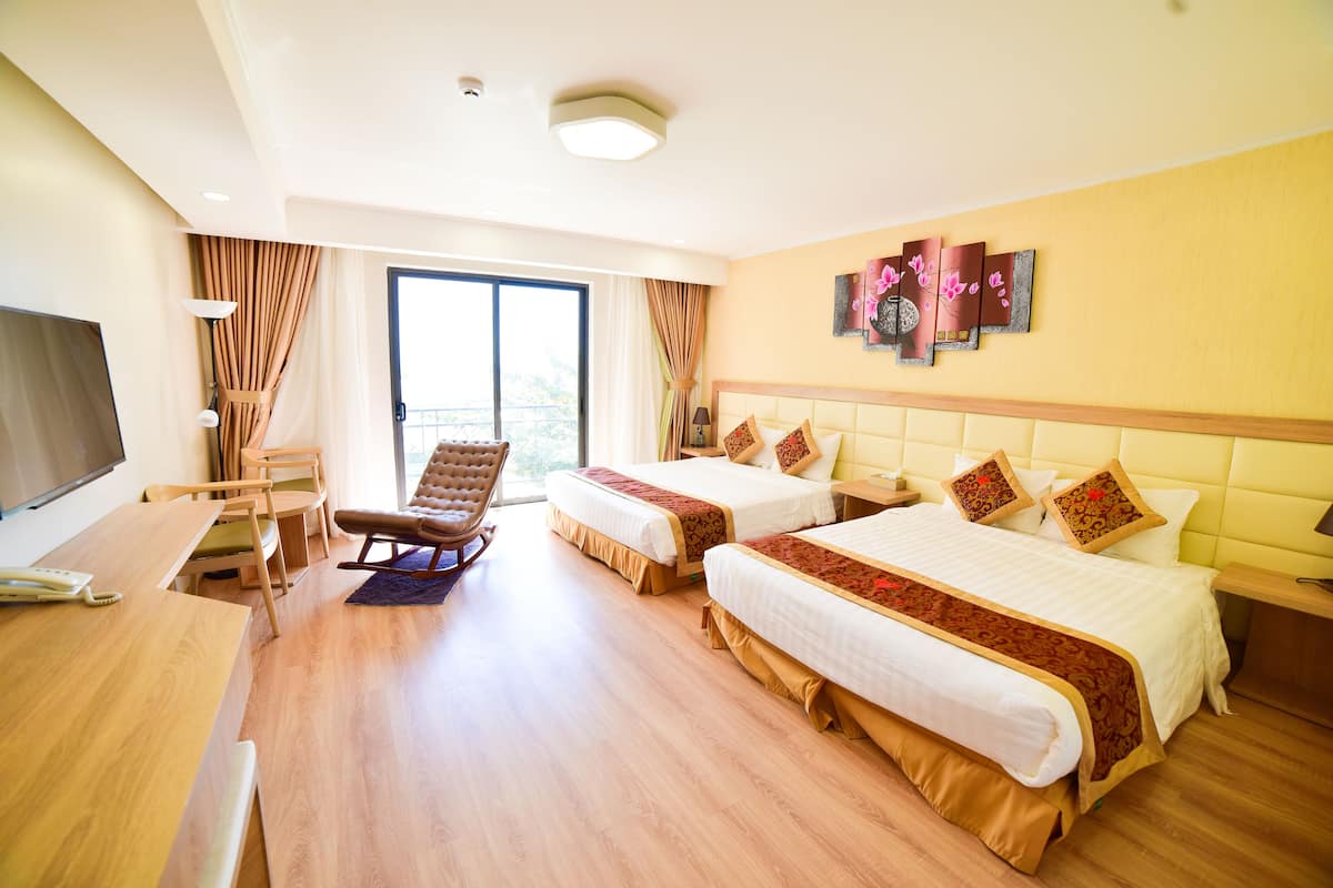 A hotel room with two beds, a desk, a chair, and a TV.