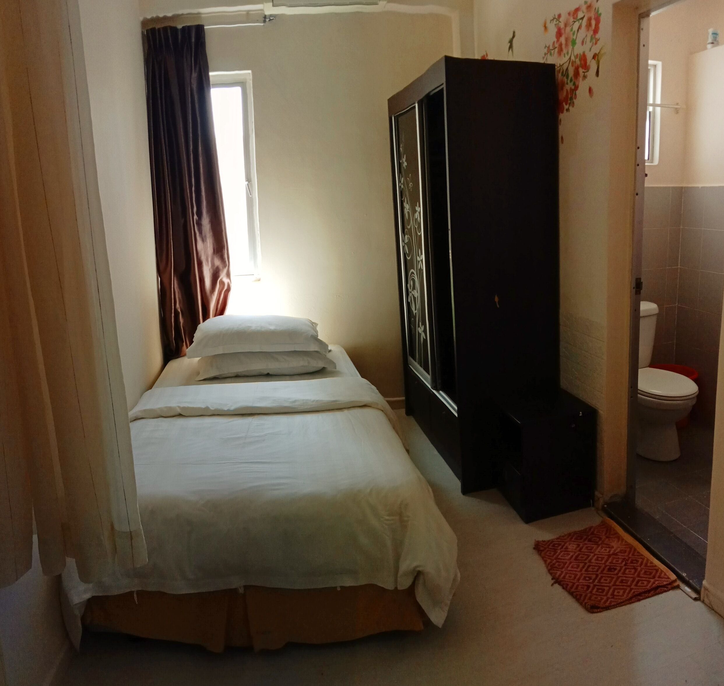 A bedroom with a bed, a wardrobe, a window with curtains, and a bathroom with a toilet.