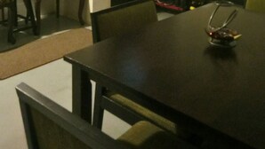 Ein Essbereich mit Tisch, Stühlen, einem Fernseher und einem Schild mit der Aufschrift 'KELUAR'.