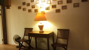 Ein Zimmer mit einem Tisch, zwei Stühlen, einem Standventilator und einer Wand mit kleinen gerahmten Bildern.