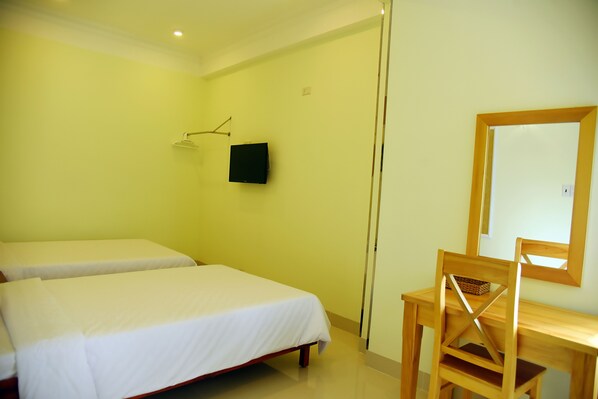 A room with two beds, a wooden desk, a chair, a wall-mounted TV, and a mirror.