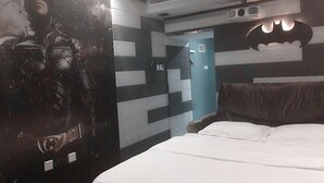 A hotel room with a bed, a wall with a Batman poster, a blue door, and a ceiling with air vents. - Cinema Hotel UIBE (Beijing)
