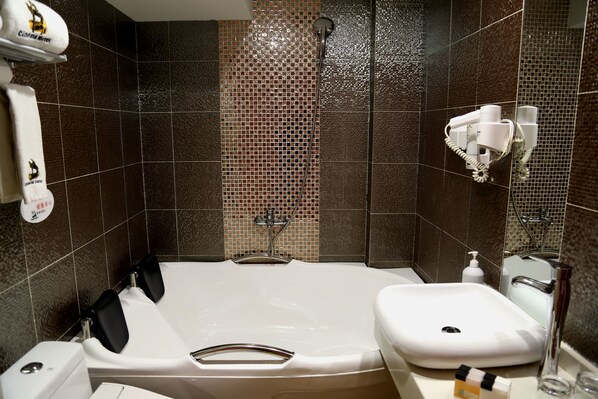 A bathroom with a bathtub, a sink, and a shower. There are hand dryers and a soap dispenser on the wall.