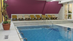 Ein Swimmingpool mit lila Wand und Holzliegen.