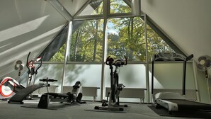 Ein Fitnessraum mit Trainingsgeräten, großen Fenstern und einer geneigten Decke.