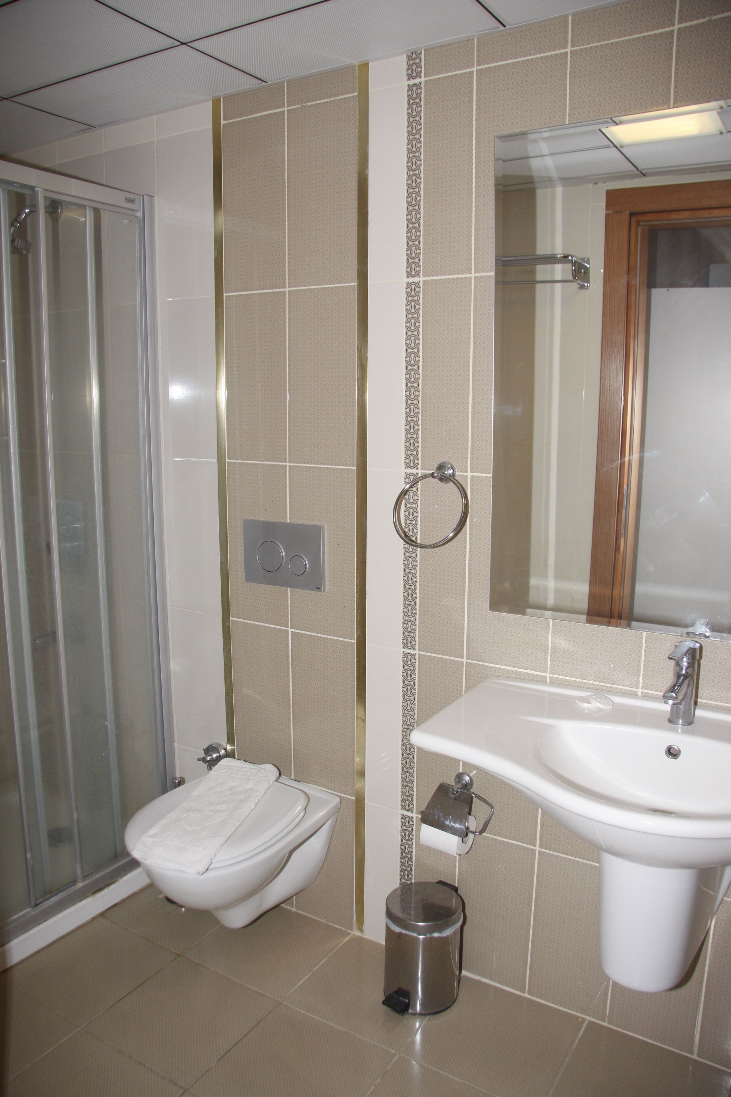 Un baño con cabina de ducha de vidrio, inodoro, lavamanos con espejo y cubo de basura.