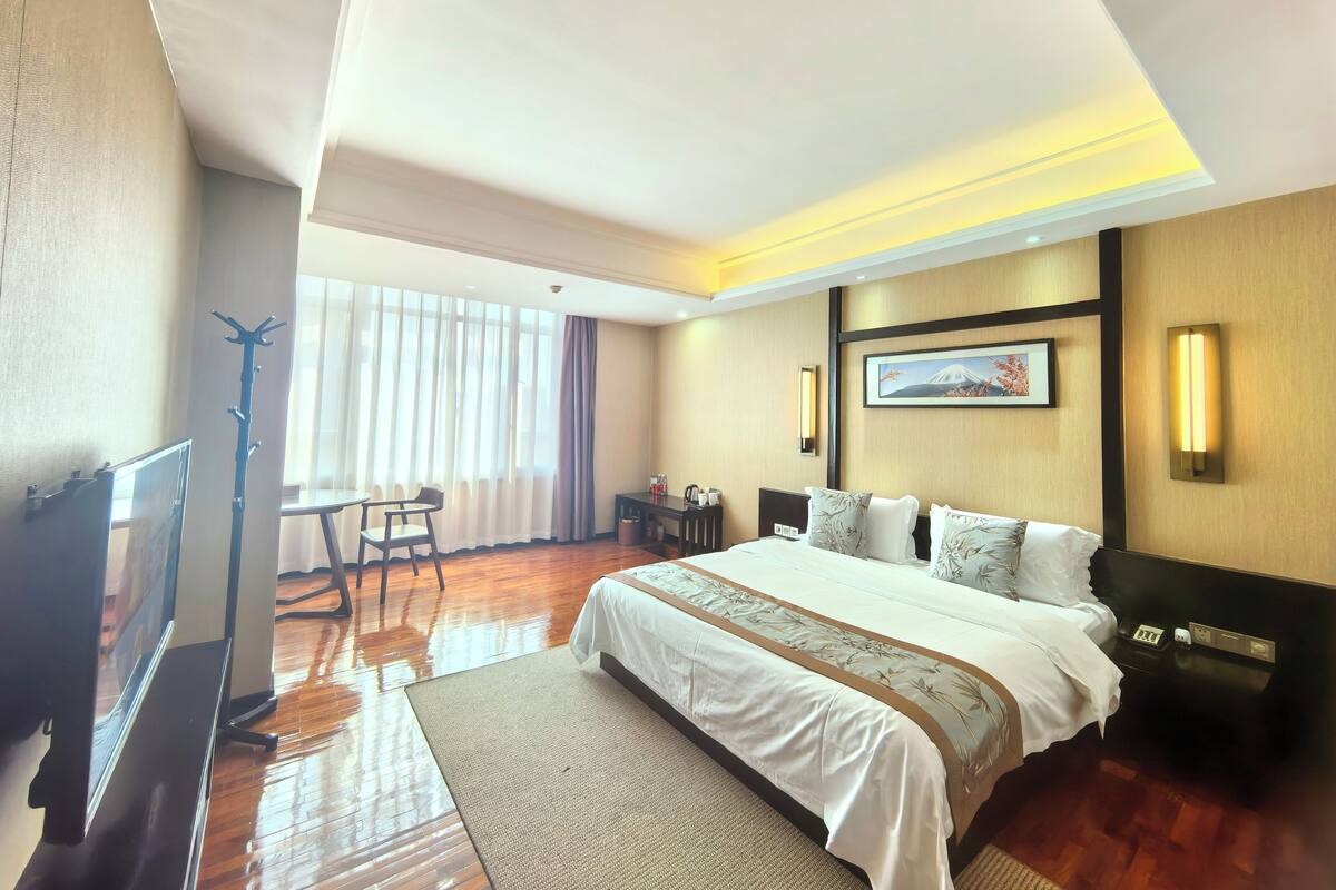 A hotel room with a large bed, a desk, a chair, and a coat rack.