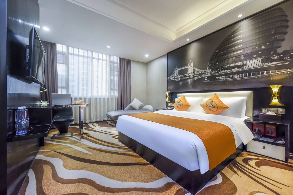 A hotel room with a large bed, a flat-screen TV, a desk, and a view of a cityscape.