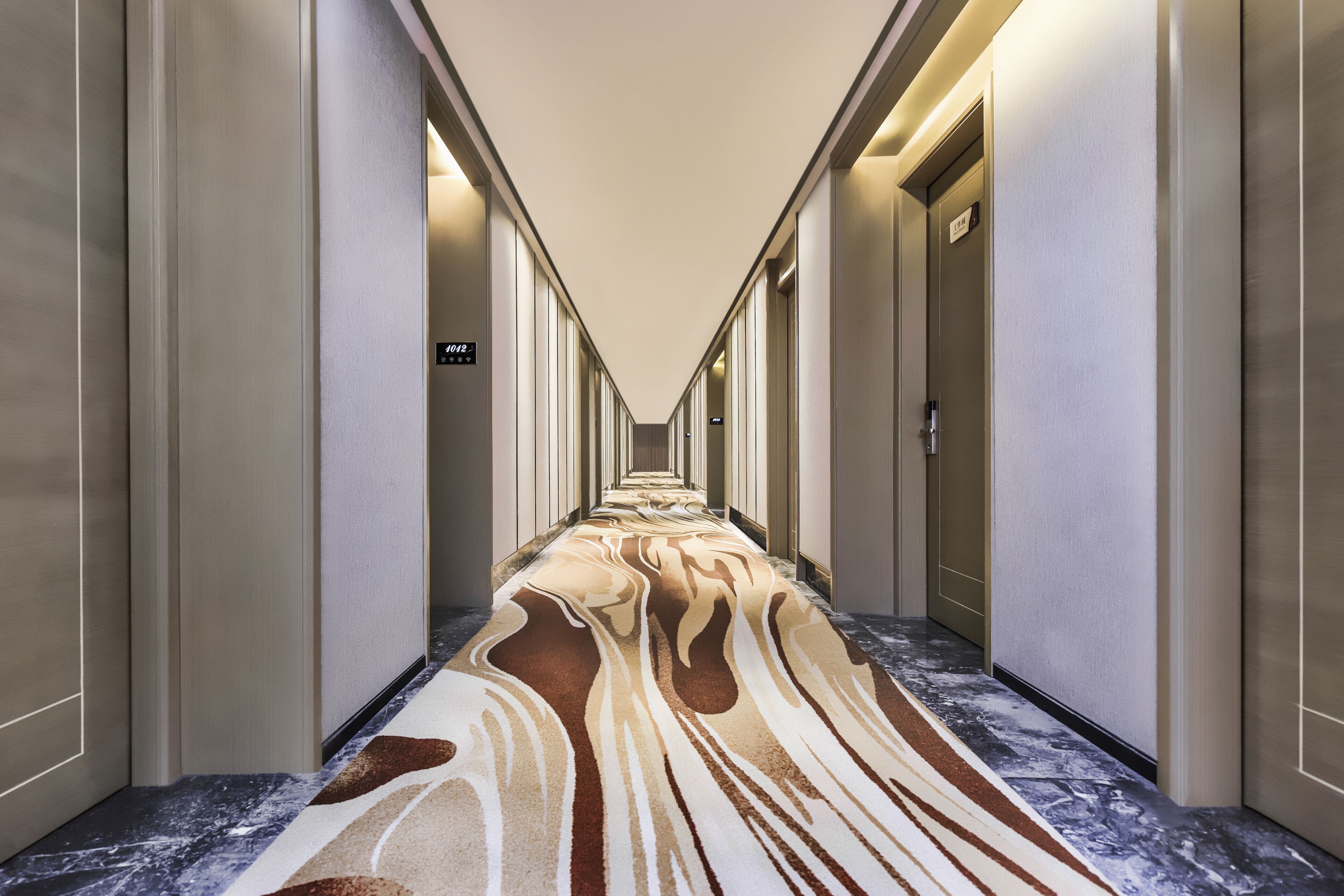 Un couloir d’hôtel avec un tapis à motifs, des portes des deux côtés et un panneau indiquant le numéro de chambre 2012.