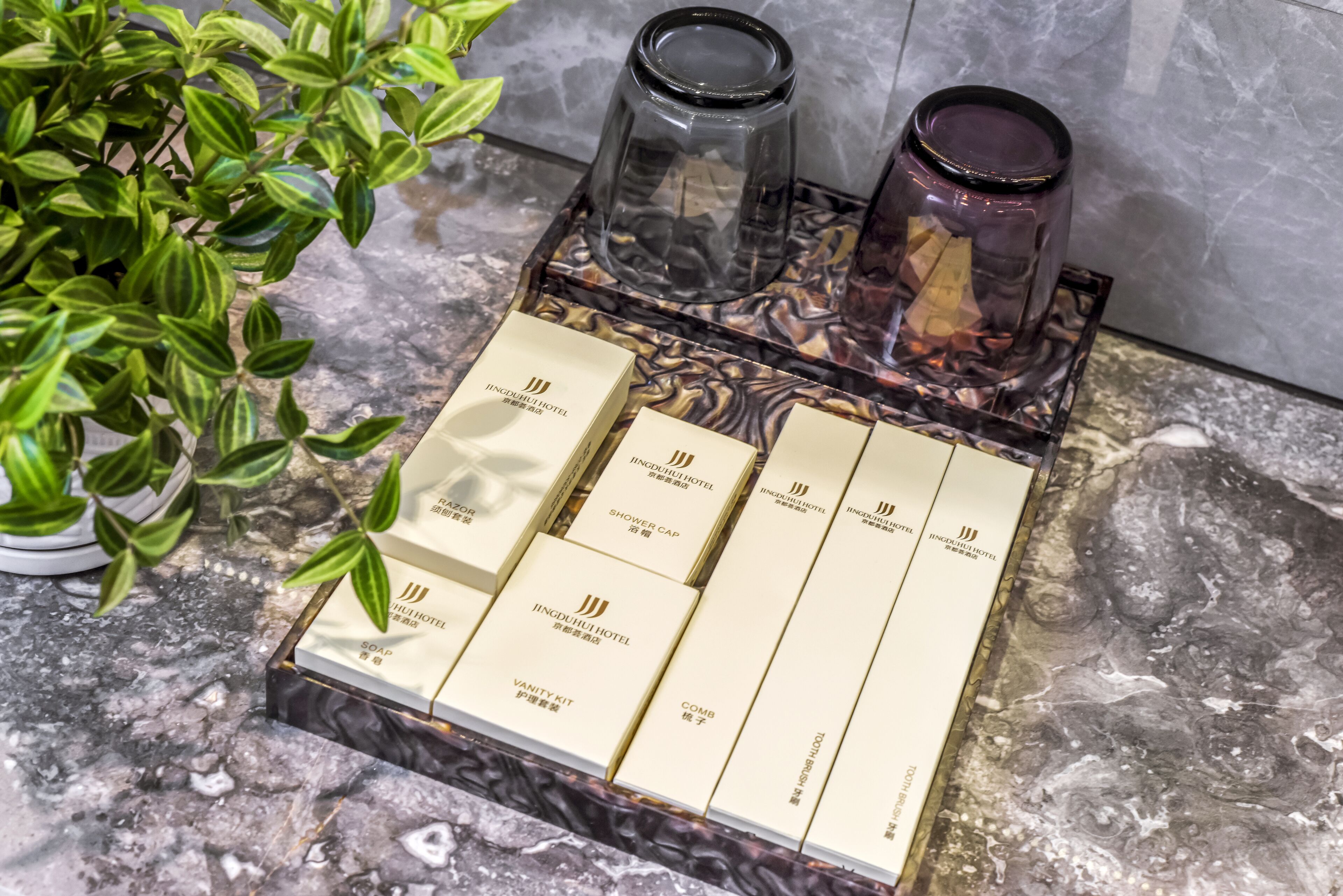 A bathroom vanity with a marble countertop, a plant, and a set of toiletries including a vanity kit, comb, and shower cap.