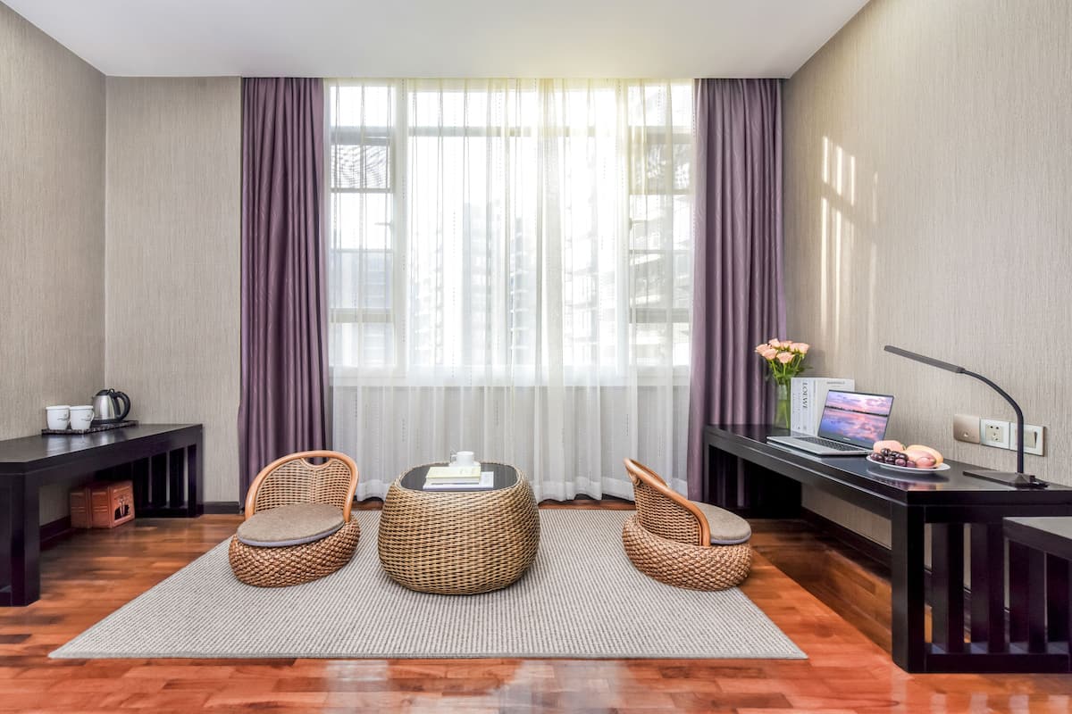 A modern room with a large window, a desk with a laptop, wicker chairs, and a small table with a vase of flowers.