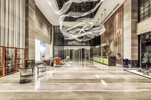 Een ruime lobby met een hoge plafond, modern meubilair en een opvallende hanglamp.