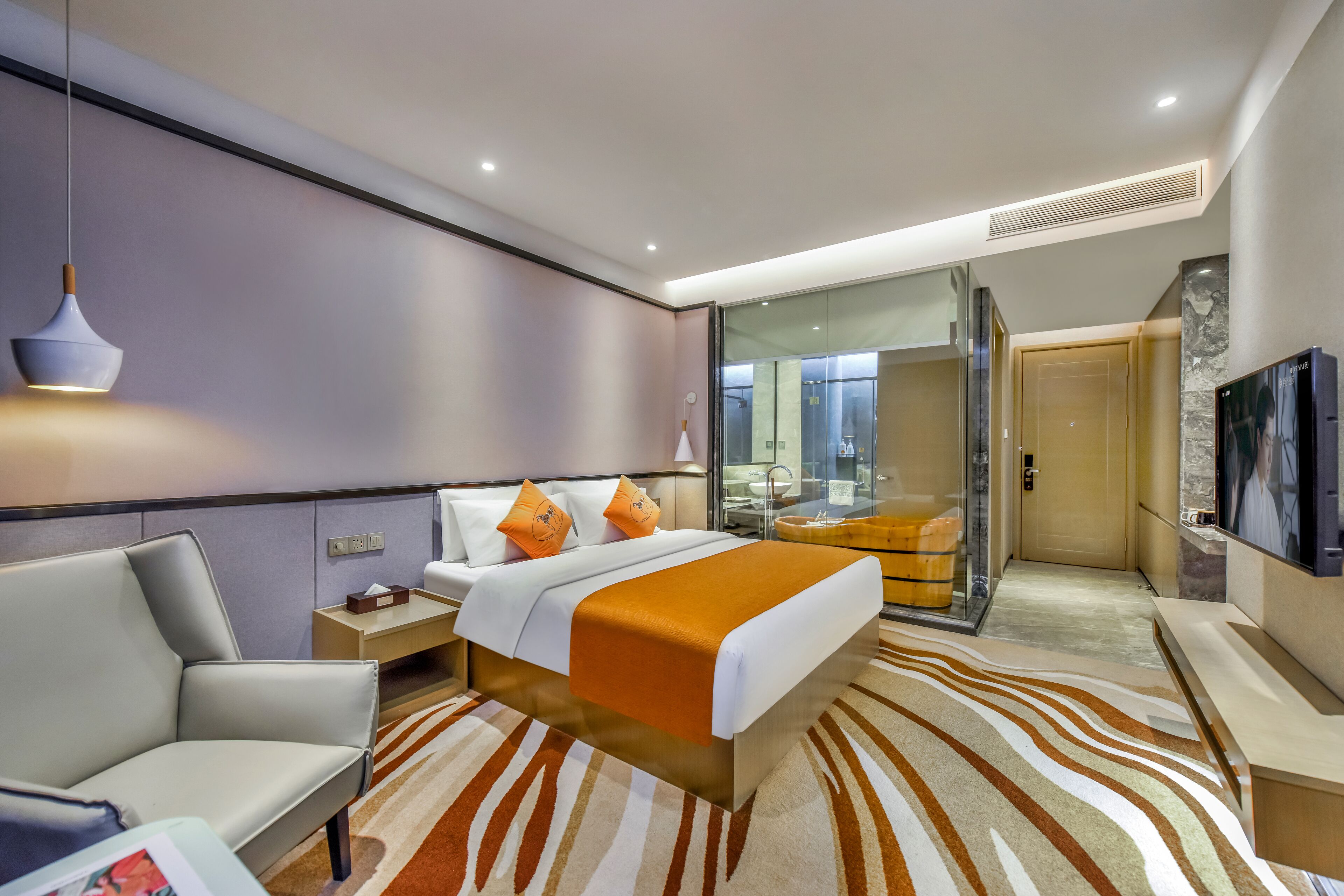 A modern hotel room with a bed, a seating area, a bathroom with a glass shower, and a TV.