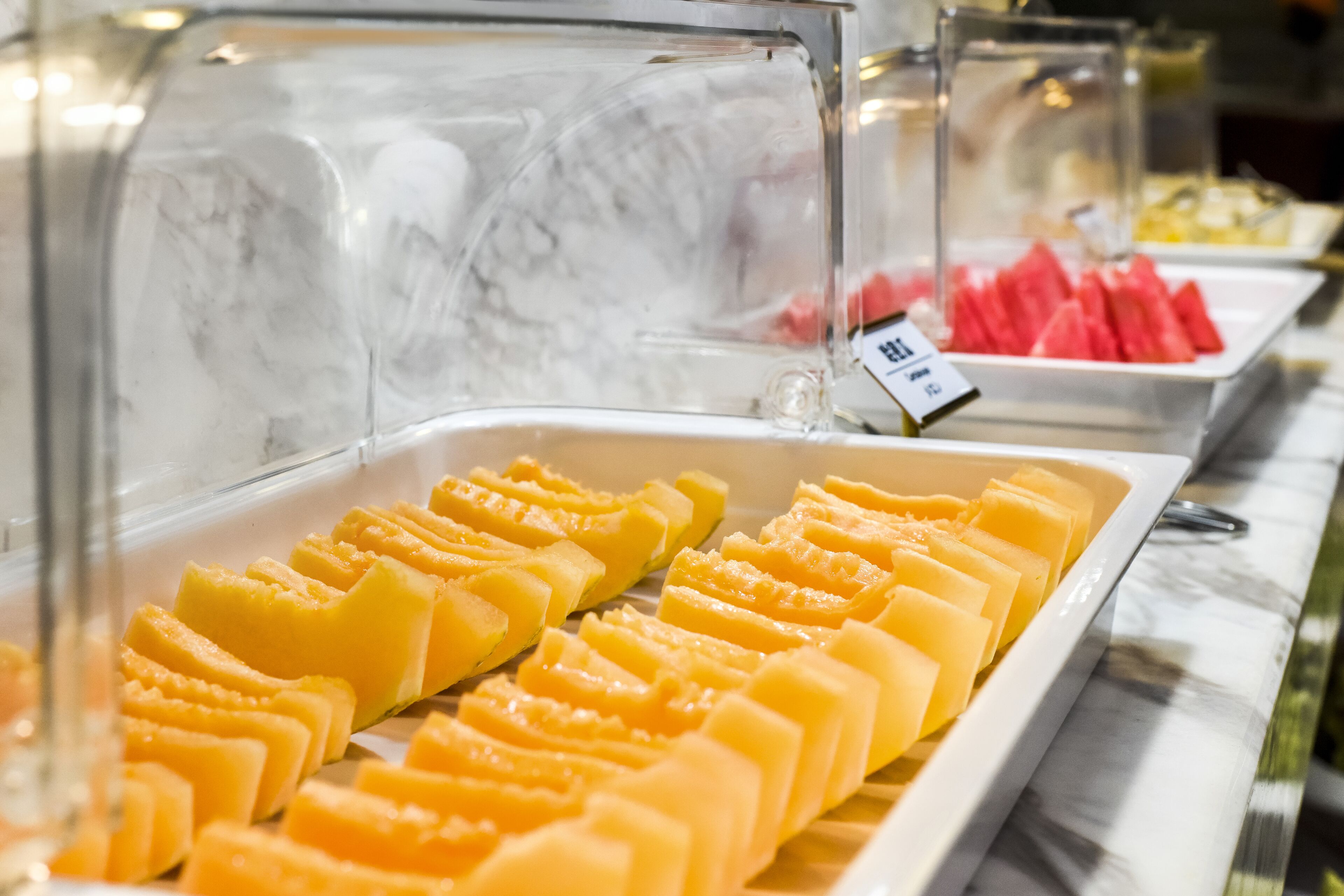 A buffet with various food items, including sliced mangoes and watermelon.
