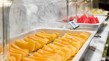 A buffet with various food items, including sliced mangoes and watermelon.